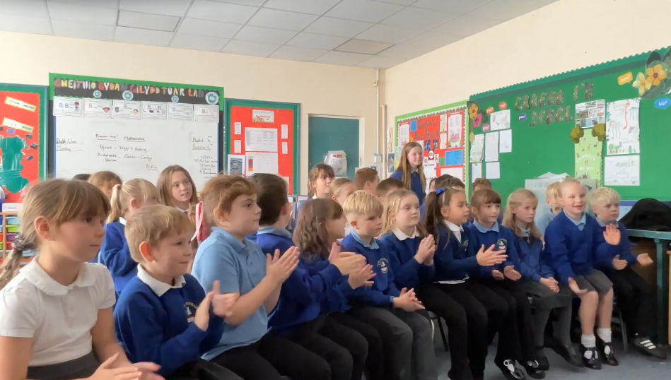 Cemaes Bay Primary School students applaud as classmate Isabelle Hughes (standing in the back) is told her patch was chosen for the parabolic flight. 