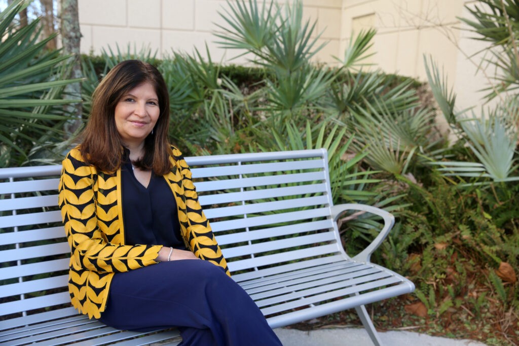 A photo of a woman sitting down on a bench smiling.
