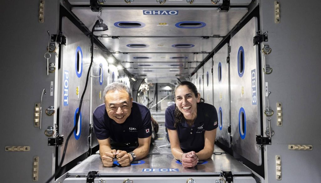 Two smiling people crawling inside a narrow hallway of the space module.